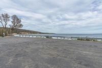 an empty parking lot on the side of the ocean shore with a bench sitting in the shade