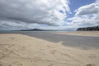 a lone beach with a large expanse of sand in the foreground and clouds above