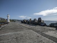 a lighthouse with rocks lining a concrete walkway next to the ocean and sky in the distance