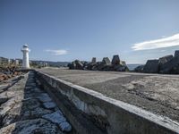 a brick walkway by the ocean and a lighthouse in the distance, with rocks and boulders scattered on the ground