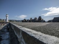 a brick walkway by the ocean and a lighthouse in the distance, with rocks and boulders scattered on the ground