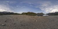 an oval fish eye view of the sky and water at a beach with small rocks and mountains