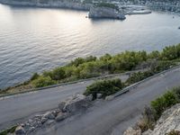 an asphalt road beside a body of water and a cliff near the shore with trees on the sides