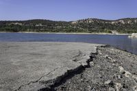 a rocky beach sitting on top of a lake near a mountain in the distance and trees