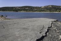 a rocky beach sitting on top of a lake near a mountain in the distance and trees