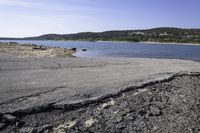 a rocky shore along a lake with mountains in the distance, with dirt and rocks strewn on the beach