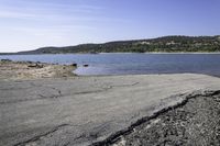 a rocky shore along a lake with mountains in the distance, with dirt and rocks strewn on the beach