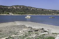 an empty beach with some water and rocks in the distance, with mountains in the background