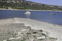 an empty beach with some water and rocks in the distance, with mountains in the background