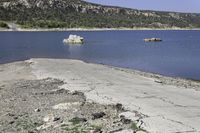 an empty beach with some water and rocks in the distance, with mountains in the background