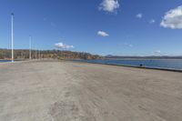 an empty parking lot is empty by a water way and two large poles are standing next to the lake