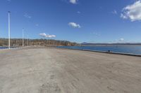 an empty parking lot is empty by a water way and two large poles are standing next to the lake