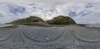 two mountain peaks are pictured next to the ocean as clouds float over them near the shore