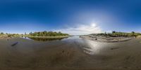 an empty body of water near many trees and sandbanks with a sunburst behind it