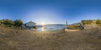 the sun sets in the horizon over the ocean, with a house and a boat nearby