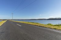 the asphalted road beside the large body of water with power lines running alongside it