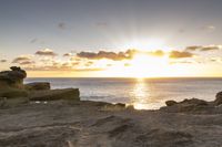 a view over the ocean from a cliff on the beach with the sun rising behind the clouds