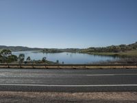 an empty road with view to a lake and a mountains in the distance, on a clear day