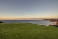 a golf course with the ocean in the background at sunset near a sandy beach with no people