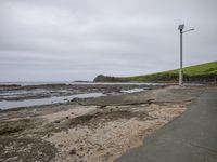 a sandy path that extends into the ocean with rocks around it, and grass in the background