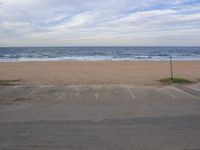 parking lot overlooking a sandy beach and ocean, with a few cars parked by the end of it