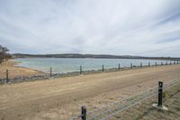 a road with a fence, next to a body of water, and the sky