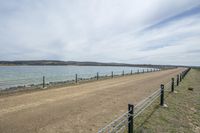 a road with a fence, next to a body of water, and the sky