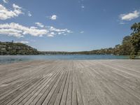 there is a wood deck by the water on this sunny day with a blue sky above