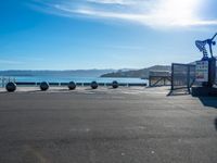 an empty parking lot with several metal balls on the concrete surface and blue water in the background