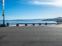 an empty parking lot with several metal balls on the concrete surface and blue water in the background