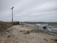 the sandy shore is surrounded by water and rocks, with a light pole in the background