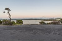 two people sitting on a road at sunset next to water and mountains in the distance