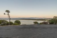 two people sitting on a road at sunset next to water and mountains in the distance