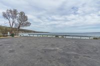 an empty parking lot sits beside the ocean and water with trees in it and two parked cars