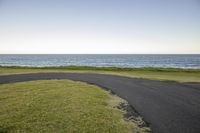 a paved pathway near the ocean by the beach as seen from the golf course area