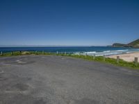 a paved road and beach next to the water on a sunny day with no clouds