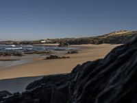 a beach area with several large rocks and water surrounding it and the water crashing over the shore