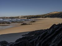 a beach area with several large rocks and water surrounding it and the water crashing over the shore