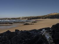 a beach area with several large rocks and water surrounding it and the water crashing over the shore