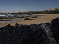 a beach area with several large rocks and water surrounding it and the water crashing over the shore