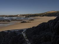 a beach area with several large rocks and water surrounding it and the water crashing over the shore