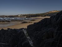 a beach area with several large rocks and water surrounding it and the water crashing over the shore