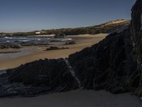 a beach area with several large rocks and water surrounding it and the water crashing over the shore