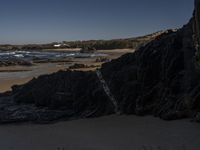 a beach area with several large rocks and water surrounding it and the water crashing over the shore