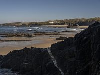 a beach area with several large rocks and water surrounding it and the water crashing over the shore