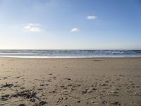 a person riding a skateboard on top of a beach next to the ocean under a blue sky