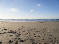 a person riding a skateboard on top of a beach next to the ocean under a blue sky