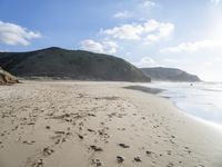 footprints make the sand near the beach in front of a mountain top and hills in the distance