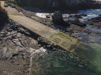 a walkway that leads to the water between the beach and rocks near a shoreline with a rock lighthouse behind it