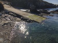 a walkway that leads to the water between the beach and rocks near a shoreline with a rock lighthouse behind it